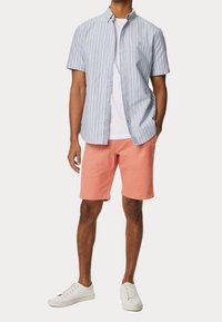 Chemise à manches courtes à rayures bleu et blanc, associée à un short corail. Le mannequin porte des baskets blanches ; design simple avec une coupe droite.