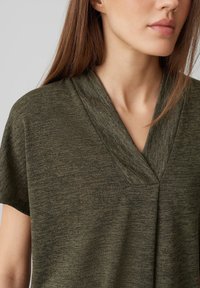 Top verde a maniche corte realizzato in tessuto a trama con scollatura a V; presenta sottili varianti tonali e una vestibilità morbida.