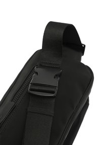 Borsa a spalla in tessuto nero con texture liscia, dotata di chiusura con zip e fibbia in plastica su una tracolla tessuta. Design compatto e angolare.
