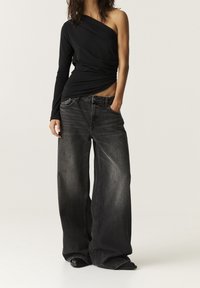 Zwarte lange mouwen top met een asymmetrische halslijn, gecombineerd met oversized zwarte jeans met een vervaagde afwerking en voorzakken.