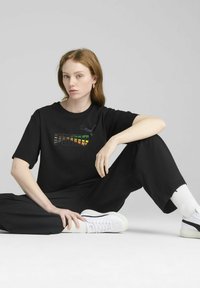 Sort t-shirt med farverig "PUMA" logo, afslappet pasform. Båret med sorte vide bukser og hvide sneakers, med et enkelt design.