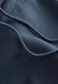 Weicher, dunkelblauer Stoff mit einer glatten Textur, der subtile Kurven und Nähte im Material aufweist und das geschichtete Design hervorhebt.