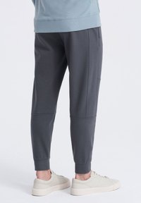 Pantalones de chándal grises hechos de una tela suave, con pierna ajustada, bolsillos laterales y puños acanalados, combinados con zapatillas de color claro.