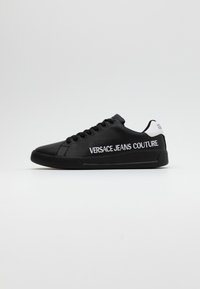 Svarta lädersneakers med svarta snören och en vit accent på hälen. Har logotypen "VERSACE JEANS COUTURE" i vitt på utsidan.