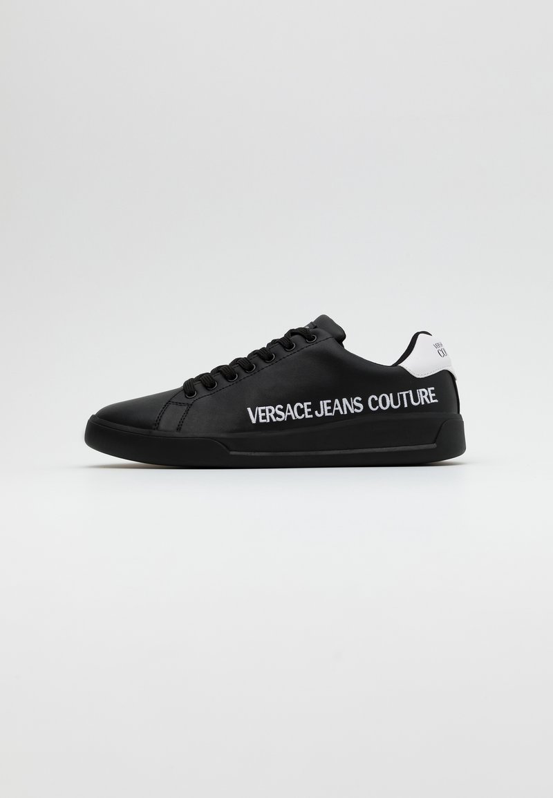 Svarta lädersneakers med svarta snören och en vit accent på hälen. Har logotypen "VERSACE JEANS COUTURE" i vitt på utsidan.