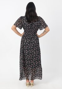 Zwart bloemen maxi-jurk met korte puffmouwen, gesmokt taille en doorzichtige stof. Bevat kleine roze en witte bloemenpatronen verspreid over de jurk.