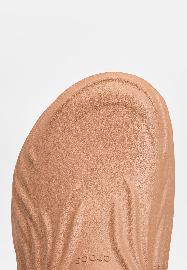 Zoccoli Crocs color tan con superficie testurizzata e design ondulato; il tallone presenta un bordo leggermente rialzato e il logo sul lato.