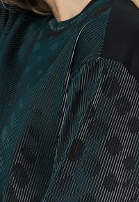 Tkanina w czarno-miętowym wzorze, prezentująca pionowe linie oraz kropki, o gładkiej fakturze i kontrastowych, czarnych akcentach na ramieniu.