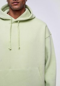 Mintgroene hoodie met een losse pasvorm, trekkoord capuchon, kangoeroezak en geribbelde zoom. Gemaakt van zachte, gestructureerde stof.