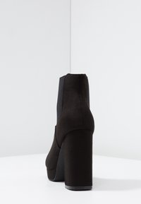 Botines negros de tacón alto con acabado de ante suave, presentando un tacón grueso y paneles laterales elásticos para una silueta elegante.