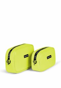 Zwei rechteckige Kosmetiktaschen in leuchtendem Gelb mit glänzenden Oberflächen, gerippter Textur und schwarzen Reißverschlüssen mit Logoakzenten.