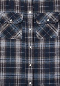Camicia di flanella con motivo a quadri blu navy, blu e grigio, due tasche anteriori e bottoni a pressione argento al centro.