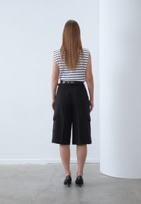 Mustat cargo-shorts, leveälahkeiset, teksturoitu kangas, jonka sivutaskut. Yhdistetty raitapaidan kanssa, ilman hihoja. Minimalistinen muotoilu vyöllä.