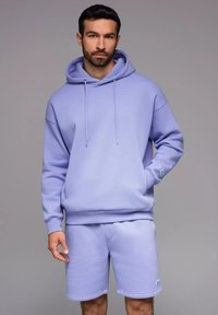 Haut en coton violet avec capuche à cordon de serrage, manches longues et poche kangourou, assorti à un short violet avec poches latérales.