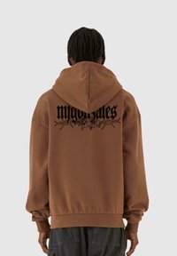 Felpa marrone con una grande grafica nera della parola "midnightsales" e dettagli floreali sul retro. Presenta un cappuccio regolabile e polsini a costine.