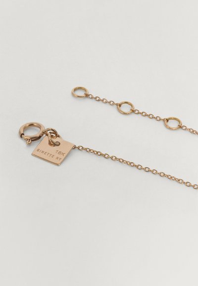 18K arany nyaklánc, amely finom láncból áll, kör alakú láncszemekkel és egy téglalap alakú címkével, amelyen a "GINETTE NY" felirat található.