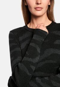 Black ribbed long-sleeve shirt with a subtle dark gray animal print. Features a rounded neckline and fitted cuffs, made of soft knit fabric.