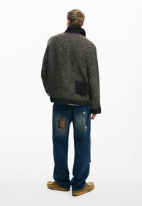 Texturierte, mehrfarbige Wollmischjacke mit hohem Kragen, kombiniert mit ausgewaschenen Jeans aus Denim mit Patches und Rissen.