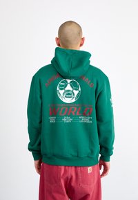 Green hoodie with a large soccer ball graphic and text on the back. Features red accents and a kangaroo pocket. Made from soft material.