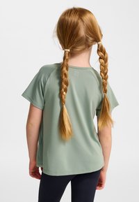 Mintgrön t-shirt med korta ärmar, lös passform och rundad fåll. Baksidan visar två flätade hårsektioner som avslöjar en mjuk textur.