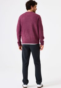Gebreide bordeauxrode trui met een ronde hals en geribbelde manchetten, gecombineerd met donkere broek en witte sneakers. Zachte textuur en een relaxte pasvorm.