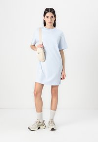 Svijetloplave oversized pamučne haljine majice s kratkim rukavima, uparene s bež Nike torbom preko ramena i sivim Nike patikama.