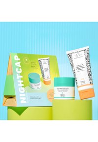 Green and blue packaging displays two skincare products: a cream in a jar with a turquoise lid and a cleanser tube with black patterns.