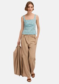 Top senza maniche azzurro chiaro con pois marroni, scollo quadrato e orlo peplum. Abbinato a pantaloni a gamba larga beige e sandali marroni.