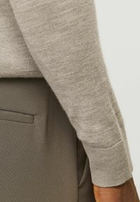 Manica di maglione a maglia beige con polsini a costine, abbinata a tessuto grigio chiaro liscio con tasca laterale. Design texturizzato e aderente.