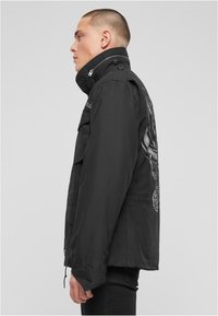 Černá lehká bunda s vysokým límcem, zipovým a knoflíkovým zapínáním a grafickým motivem na zádech. Obsahuje několik kapes.