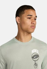 Camisa de manga larga verde claro con un gráfico de baloncesto y texto "Nike". Tejido suave y liso con un cuello redondo y un corte relajado.
