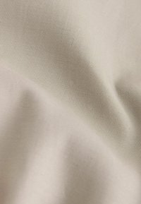 Mjuk, beige tyg med fin diagonalt ribbad textur och mjuka veck som skapar subtila ljus- och skuggvariationer.