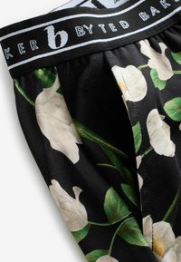 Czarne szorty z materiału z kwiatowym wzorem białych kwiatów i zielonych liści, z kontrastującym pasem oznaczonym "b by Ted Baker."