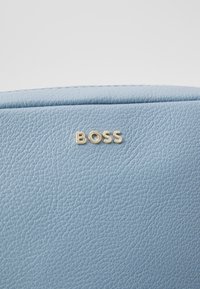 Borsa in pelle testurizzata azzurro chiaro con logo "BOSS" in tonalità oro stampato sulla superficie. Finitura liscia con dettagli di grana delicati.
