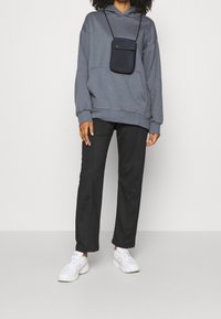 Sweat à capuche gris avec une poche avant, associé à un pantalon noir droit et des baskets blanches. Tissu lisse, design décontracté.
