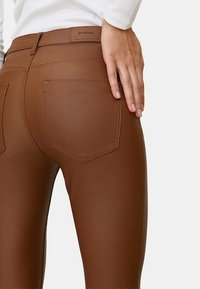 Bruine legging van rekbaar materiaal. Bevat een hoge tailleband, twee achterzakken en contrasterende stiksels. Soepele textuur.