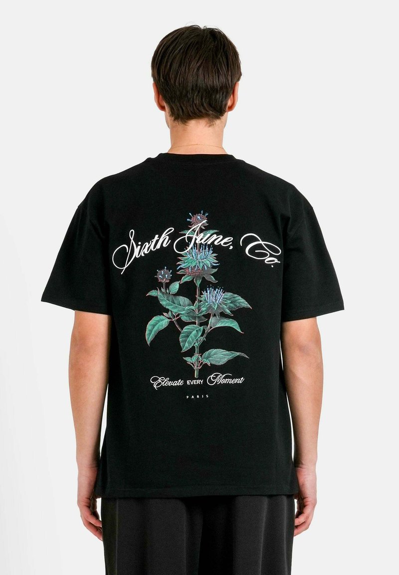 Svart bomull t-shirt med en färgglad blommig grafik på baksidan, med vit text och detaljer. Kort ärm och avslappnad passform.