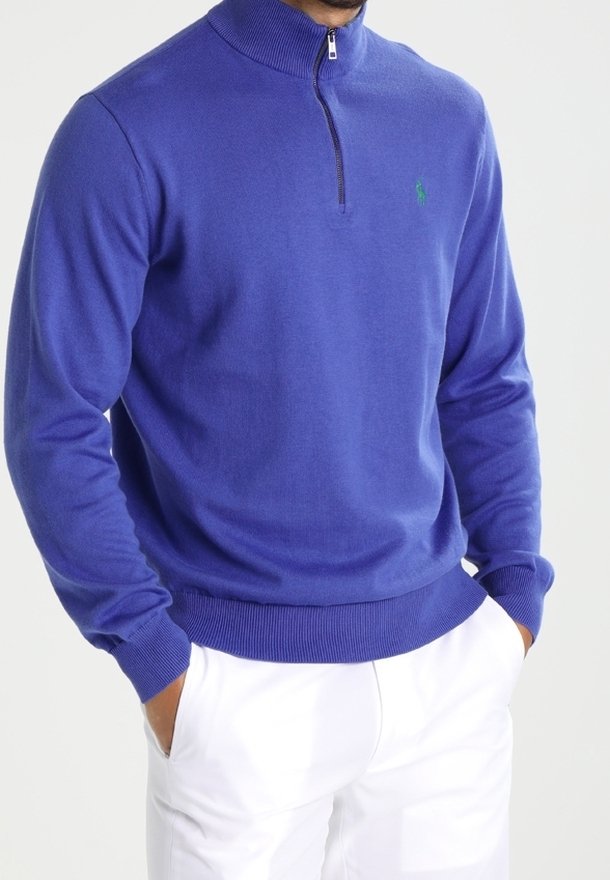 Pull bleu royal avec un col haut et une fermeture éclair, doté de poignets et d'un ourlet côtelés, mettant en valeur un logo vert sur la poitrine.
