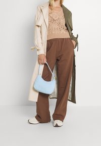 Beige trenchcoat över en stickad persikofärgad topp, bruna vida byxor och en ljusblå handväska. Mjuka texturer och avslappnad passform genom hela outfiten.