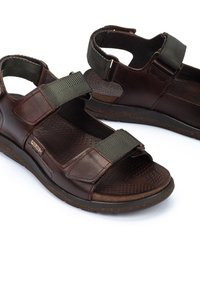 Sandalias de cuero marrón con correas de tela verde ajustables, plantilla texturizada y suela acolchada, con un diseño cosido y herrajes resistentes.