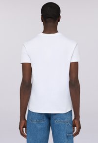 Camiseta de algodón blanca con mangas cortas y cuello redondo, vista desde atrás, combinada con jeans de mezclilla. Diseño limpio y sin adornos.