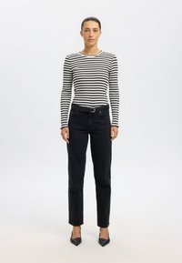 Fekete-fehér csíkos hosszú ujjú felső, magas derekú fekete farmerrel párosítva. A megjelenést fekete öv és hegyes orrú fekete magassarkú egészíti ki.