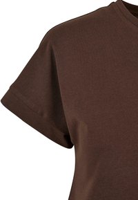 Hnědé bavlněné tričko, krátké rukávy, kulatý výstřih, hladká textura, včetně mírného lesku a detailu srolovaných rukávů.