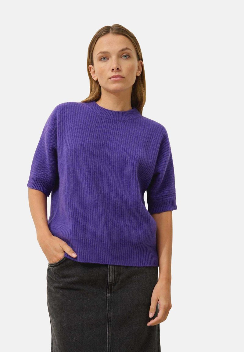 Fioletowy sweter z dzianiny z krótkimi rękawami, okrągłym dekoltem, prążkowaną fakturą, luźnym krojem, zestawiony z ciemną spódnicą.