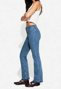 Džíny s vysokým pasem, modré denimové, s virechatým střihem, pěti kapsami a zapínáním na knoflík, v kombinaci s tmavě hnědými sandály na řemínky.