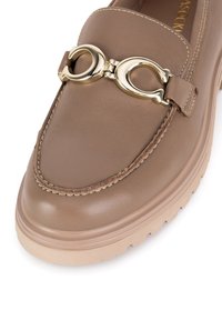 Brūni ādas loaferi ar zeltītas metāla akcentu, kuriem ir noapaļots purngala dizains, izšūtas detaļas un bieza beige krāsas zole.