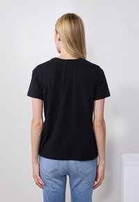 Svart bomull t-skjorte med korte ermer, med klassisk rund hals og avslappet passform, sammen med lyseblå denimjeans.