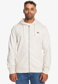 Krémová mikina na zips z mäkkej bavlnenej zmesi, s predným zipsom, nastaviteľnou kapucňou a malým logom na ľavej hrudi. Dve predné vrecká.