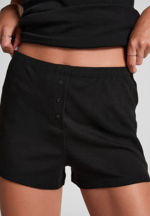 Zwarte shorts van een gestructureerde stof, met verticale strepen en een knoopsluiting met drie zwarte knopen aan de voorkant.