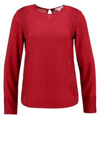 Blouse rouge à manches longues en tissu lisse, avec des détails en dentelle sur les côtés et les poignets, et une ouverture dos en forme de goutte.